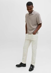 Polo a maniche corte color marrone chiaro con motivo, abbinata a pantaloni crema aderenti e scarpe eleganti nere.