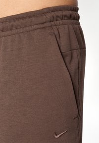 Brune bomuldsblandede sweatpants med en tekstureret overflade, elastisk talje, sidelommer og et lille broderet logo nær kanten.