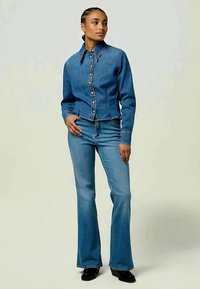 Casaco de denim com fecho de botão e colarinho pontiagudo, combinado com calças de denim flare. Ambos em azul claro, apresentando detalhes de costura sutis.