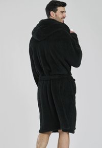 Svart huva badrock tillverkad av mjukt, strukturerat tyg med knytmidja, knälång design och fickor på sidorna.