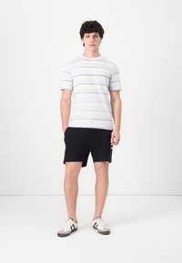 Striped short-sleeve t-shirt in light gray and navy, paired with black shorts. Model wears gray and white sneakers with black stripes.