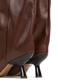 Brązowe skórzane buty na wysokim obcasie o gładkiej teksturze, charakteryzujące się eleganckim designem i kontrastującymi czarnymi akcentami na obcasie.