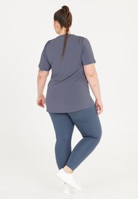 Grå t-shirt med korte ærmer, parret med blå leggings. Outfittet har en afslappet pasform, blød tekstur og et simpelt design, båret med hvide sko.