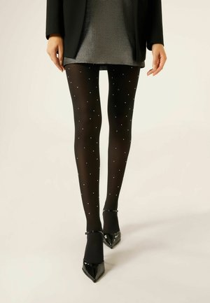 Sorte strømpebukser med en gennemsigtig finish, prydet med små sølvprikker, parret med spidse sorte hæle. Modellen bærer en metallisk grå nederdel.