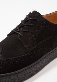 Černé semišové brogue boty s detaily na špičce, perforacemi, černými tkaničkami a texturovanou černou podrážkou.