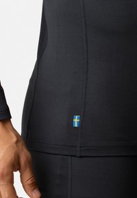 Zwarte sportshirt gemaakt van rekbaar materiaal met lange mouwen. Bevat een klein blauw en geel Zweeds vlaggetje nabij de zoom.