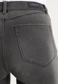 Vaqueros de denim gris descolorido con una cintura alta, que cuentan con un bolsillo trasero y una etiqueta negra con la marca "ONLY". Costura visible.
