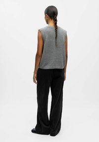 Pull gris sans manches en tricot, associé à un pantalon en velours côtelé noir à jambes larges, montrant une texture lisse et une coupe décontractée.