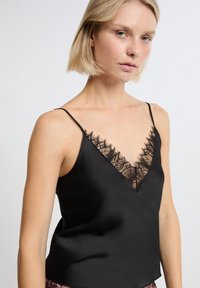 Camisola in satin nero con scollatura a V, caratterizzata da una delicata bordatura in pizzo nero lungo i bordi e spalline sottili e regolabili.