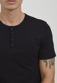 Black cotton t-shirt featuring a round neckline, five-button placket, and short sleeves. Smooth texture with visible stitching details.