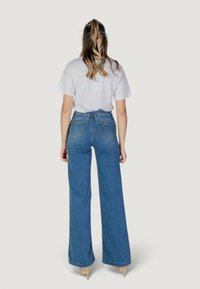Jeans de mezclilla azul de cintura alta con piernas anchas y cinturón en la cintura. Presentan bolsillos traseros y una textura suave, combinados con una camiseta blanca.