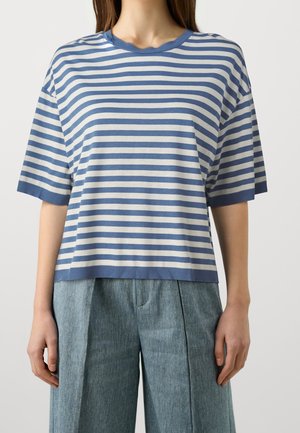 Femme portant un t-shirt à manches courtes rayé horizontalement bleu et blanc, associé à un pantalon large bleu taille haute.