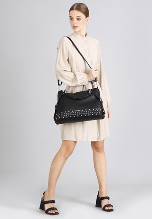 Sort imiteret læder håndtaske med sølvnitter langs den nederste front, en rund form og justerbar skulderrem.