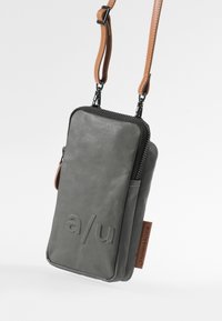 Gray fabric pouch with a textured surface, featuring a zip closure, brown leather strap, and embossed logo on the front.