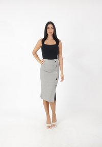 Zwart aansluitend tanktop gecombineerd met een grijze kokerrok met een zijsplit en decoratieve knopen. Het model draagt transparante haksandalen.