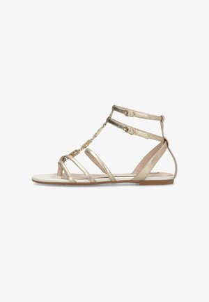 Gouden metalen platte sandalen met meerdere banden en een kettingdetail. De zool is vlak, met een gladde beige afwerking en een minimalistisch ontwerp.