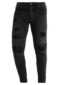 Jeans ajustados de mezclilla negra con parches desgastados y dobladillos deshilachados. Cierre de botón y cinco bolsillos. Textura suave, diseño ceñido.