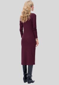 Burgundowa sukienka z długim rękawem o dopasowanej sylwetce, wykonana z prążkowanej tkaniny, zestawiona z czarnymi botkami na wysokim obcasie do kolan.