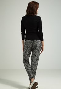 Haut noir à manches longues associé à un pantalon ajusté à motifs dans des nuances de noir et blanc. Caractérisé par une texture lisse et une hauteur à la cheville.
