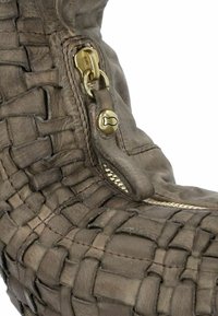 Stivale in pelle marrone con texture intrecciata, caratterizzato da una zip dorata e dettagli in metallo. La zip si estende lungo il lato per una facile vestibilità.