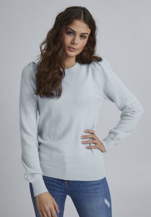Hellblaues Sweatshirt aus weichem, strukturiertem Stoff. Verfügt über einen gerippten Halsausschnitt und Bündchen sowie leicht gepuffte Ärmel. Getragen mit blauen Jeans.