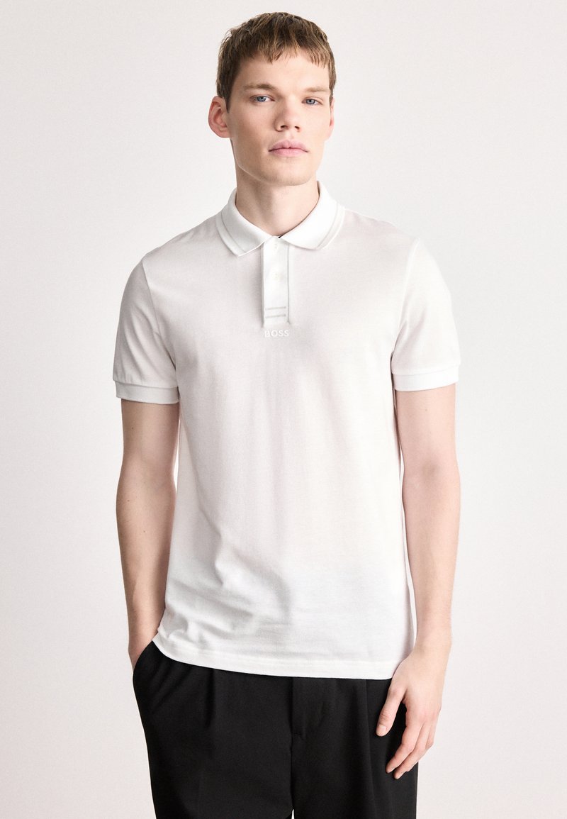 Λευκό πόλο πουκάμισο από απαλό βαμβάκι, με πατιλέτα τριών κουμπιών, κοντά μανίκια και διακριτικό λογότυπο στο στήθος.