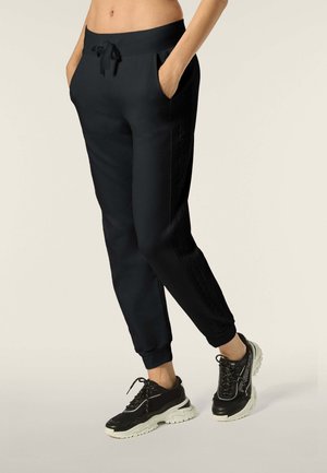 Pantaloni da jogging neri con una fascia in vita larga, cordino, tasche laterali e strisce laterali testurizzate. Abbinati a scarpe da corsa nere.