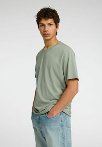 Camiseta de manga corta verde claro hecha de tela suave, con cuello redondo y corte relajado, combinada con jeans azul claro.
