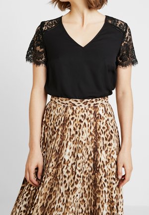 Vrouw die een zwart V-hals topje draagt met korte mouwen van kant en een hoge taille, geplooide rok met luipaardprint.