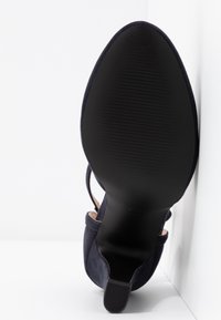 Chaussure à talons hauts en suede bleu marine, avec une semelle en caoutchouc noir lisse dotée d'un motif de bande horizontale et un design fin et pointu.