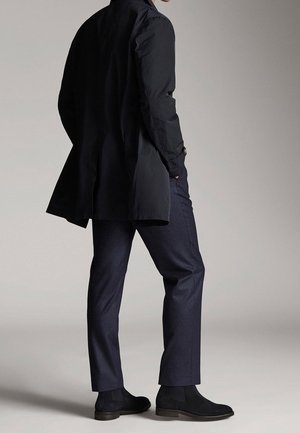 Black long coat with a tailored fit, paired with dark navy trousers and black suede ankle boots. Smooth texture and refined design.