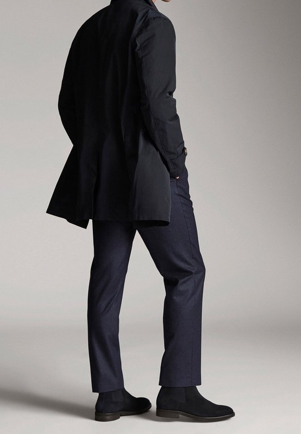 Black long coat with a tailored fit, paired with dark navy trousers and black suede ankle boots. Smooth texture and refined design.