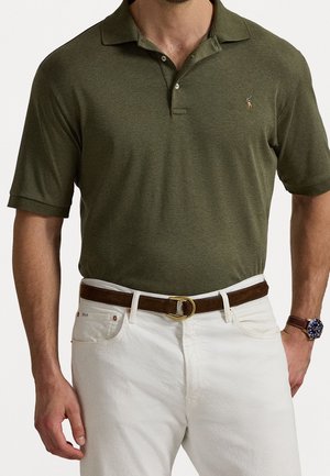 Mand iført en olivengrøn poloshirt med korte ærmer, stoppet i hvide bukser med et brunt læderbælte og et armbåndsur.