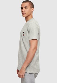 Camiseta de algodón gris con mangas cortas. Presenta un pequeño gráfico colorido de Mickey Mouse en la parte izquierda del pecho. Ajuste sencillo y relajado.