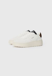 Hvite sneakers laget av semsket skinn og lær med en kraftig såle. Har en teksturert tåboks, svarte aksenter og en leopardmønstret hæltab.