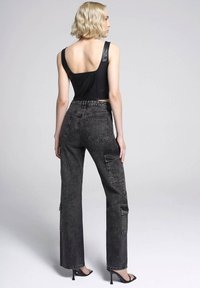 Top corto con dettagli in pelle nera, pantaloni cargo in denim scuro a vita alta con tasche e tacchi neri eleganti. Texture lisce e vestibilità sartoriale.