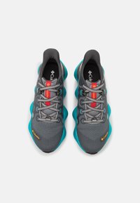 Scarpe da ginnastica grigie e turchesi con tomaia in rete traspirante, lacci rossi prominenti e suola ammortizzata. Presenta il logo Columbia.