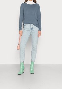 Blaues Oberteil mit langen Ärmeln, hellblaue Jeans, mintgrüne Knöchelstiefel und rosa Handtasche. Glattes Material und simples Design ohne Muster.