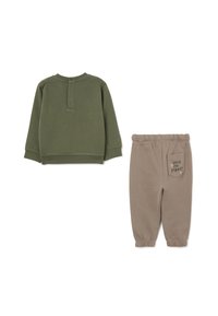 Sudadera verde oliva con cuello redondo y cierre de tres botones. Pantalones jogger beige con puños elásticos y un bolsillo trasero que presenta el texto "into the forest".