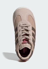 Svetlohnedá teniska s textúrovaným látkovým zvrškom, tmavohnedými pruhmi a vzorovanou gumovou podrážkou. Má polstrovaný jazyk a ružové logo.