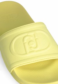Sabot galben cu o curea texturată, care are un logo reliefat, talpă netedă și o formă ușor curbată. Fabricat dintr-un material moale de cauciuc.