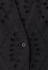 Tissu noir avec des motifs brodés de feuilles et des découpes ovales, avec un petit bouton métallique gravé "street one."