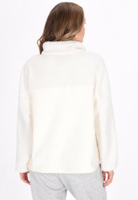 Crème-kleurige fleece pullover met een zachte textuur, uitgerust met een neklijn en een naadloos ontwerp, gecombineerd met lichtgrijze broek.