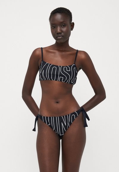 Black bikini set featuring a bandeau top and tie-side bottoms, adorned with large white lettering. Smooth texture and minimal design.