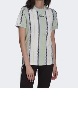 Personne portant un t-shirt Adidas à manches courtes avec des rayures verticales noires et jaunes et un écusson logo, associé à un pantalon noir avec des rayures blanches.