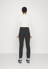 Pitkät hihat valkoinen paita ja mustat housut, joissa on tiukka malli; housuissa on vetoketjut nilkoissa, joita on käytetty mustien ja teal-väristen urheilukenkien kanssa.