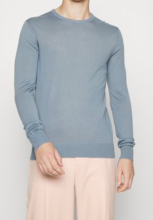 Light blue crew neck sweater in soft knit fabric. Fitted silhouette with long sleeves and ribbed cuffs and hem. Paired with light pink trousers.
