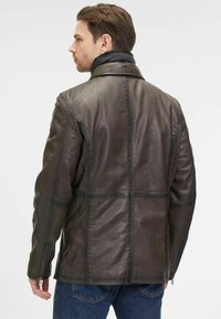Braune Lederjacke mit gestepptem Muster, Stehkragen und seitlichen Reißverschlüssen; sichtbare Nähte und Patches verleihen dem Design Details.