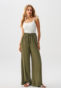 Canotta bianca abbinata a pantaloni larghi verde oliva con vita elastica e coulisse. Modello che indossa sandali chiari.