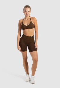 Reggiseno sportivo marrone con dettagli arricciati abbinato a shorts a vita alta coordinati. Vestibilità aderente, texture liscia e tessuto elastico.